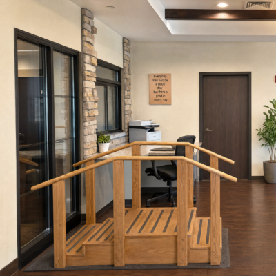 Interior view of a care center with a small wooden ramp leading to a sliding glass door, a potted plant, a sign on the wall, and office equipment near a closed door.
