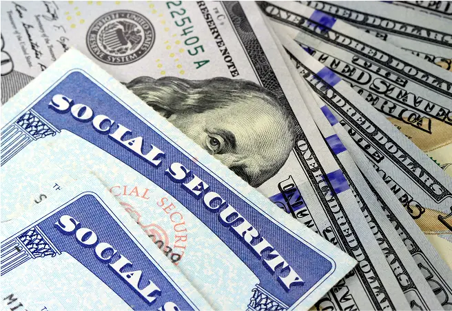 Close-up of Social Security cards placed on a pile of U.S. dollar bills, including $100 bills.